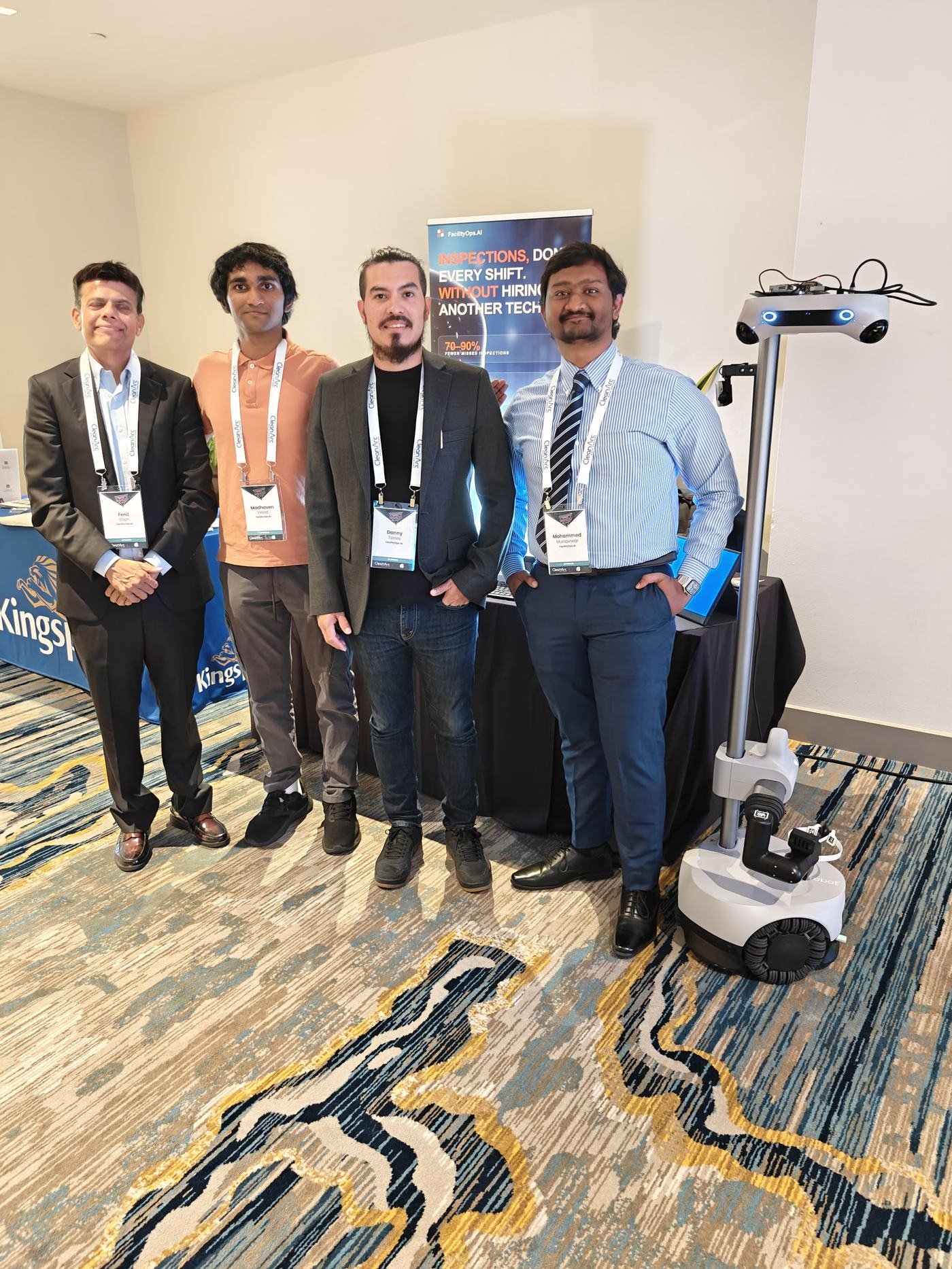People standing with an inspection robot in front of a FacilityOps booth backdrop.