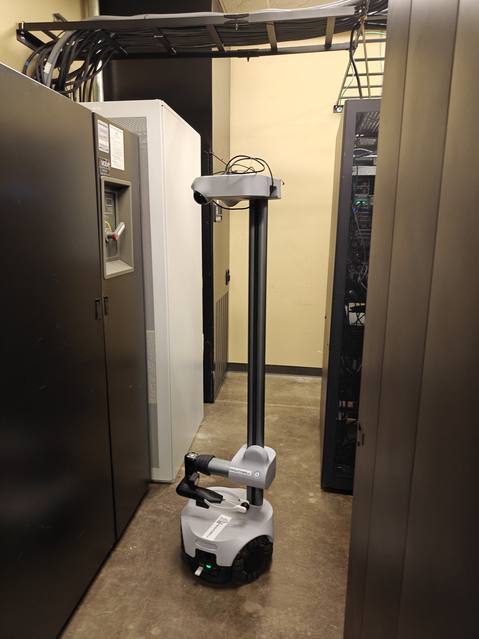 A blue and black inspection robot standing in a warehouse aisle between tall pallet racks.